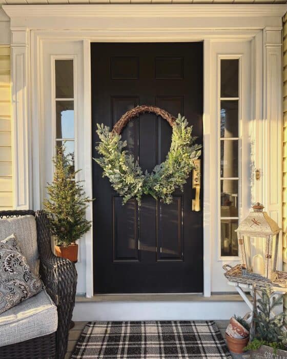Black door with winter porch decor and plaid rug